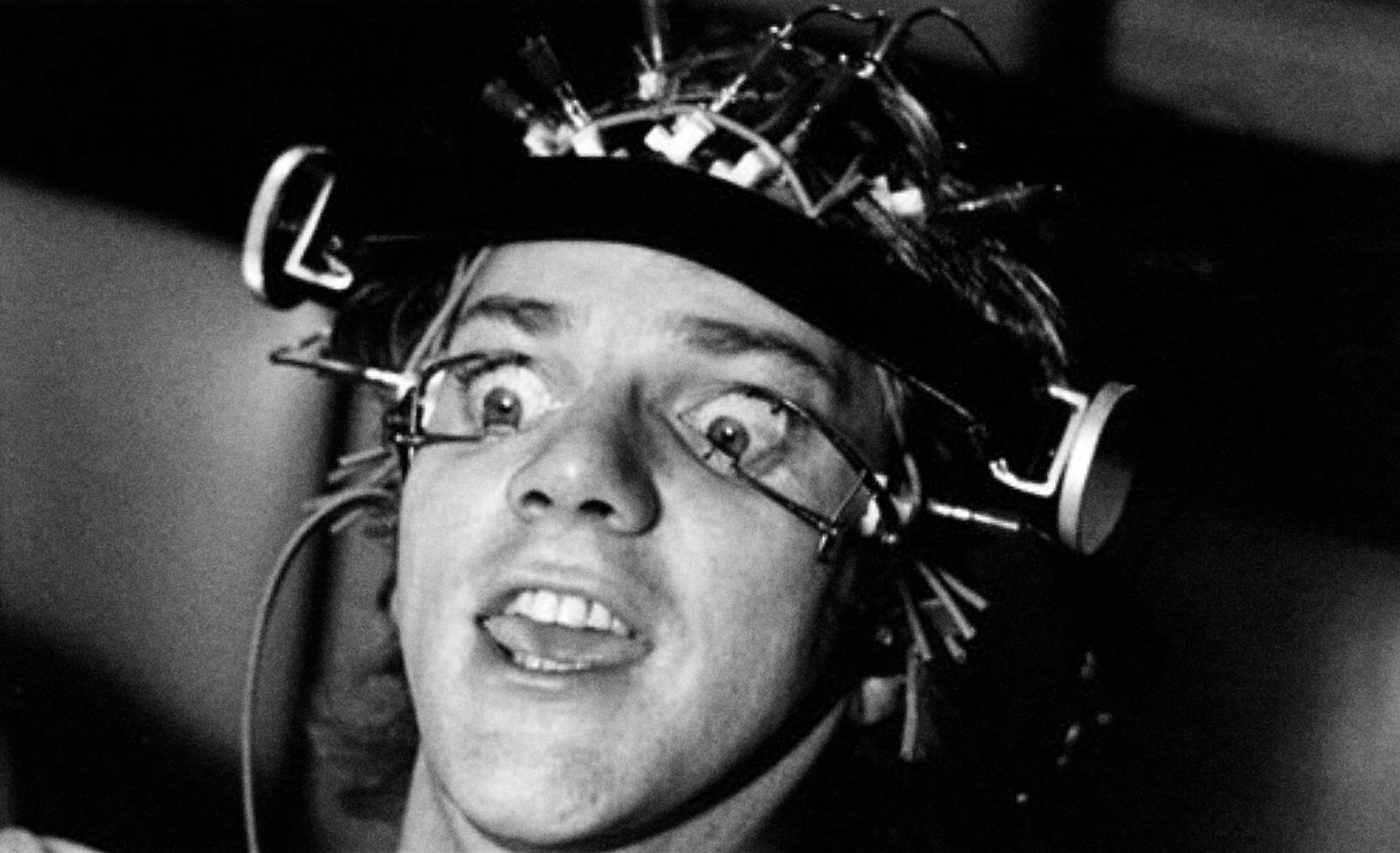 A still from the film Clockwork Orange, showing the protagonist with a contraption that keeps his eyes open. On his face an expression of bemused panic.